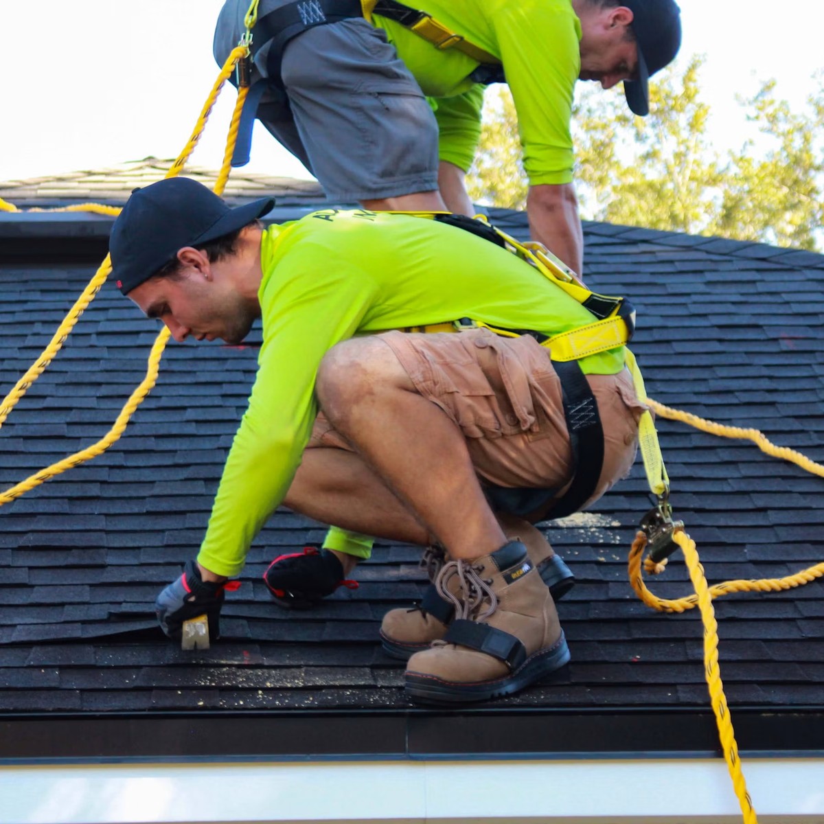 Roofing professional repairing asphalt shingles while secured with safety equipment, representing Roofing Repair services near me.