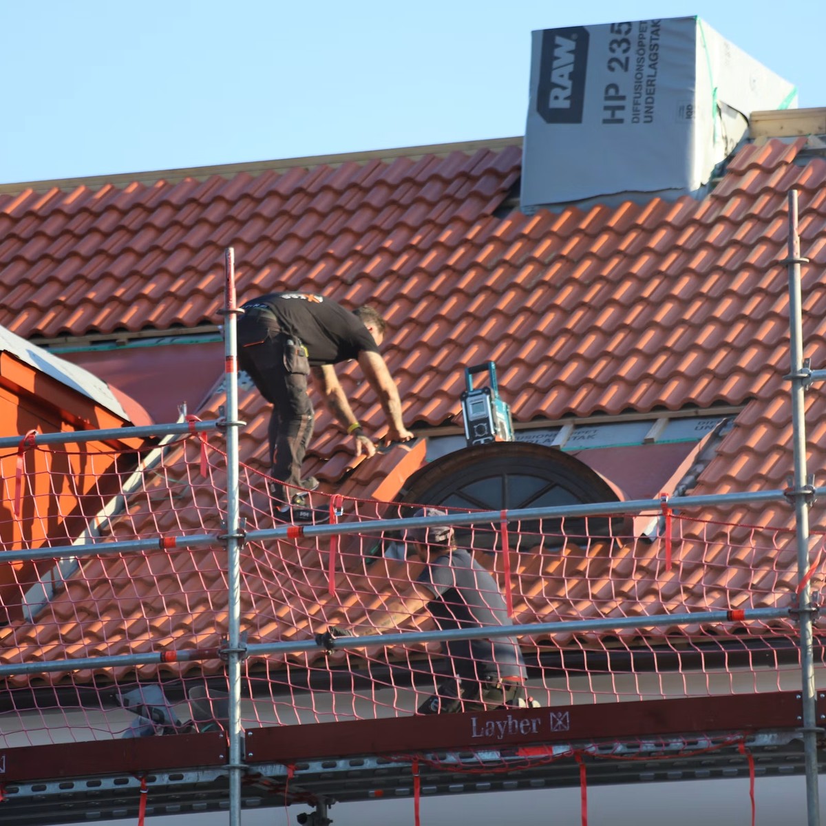 Roofing professional installing and repairing tile roofing with safety equipment in place, representing Roofing Repair services near me.