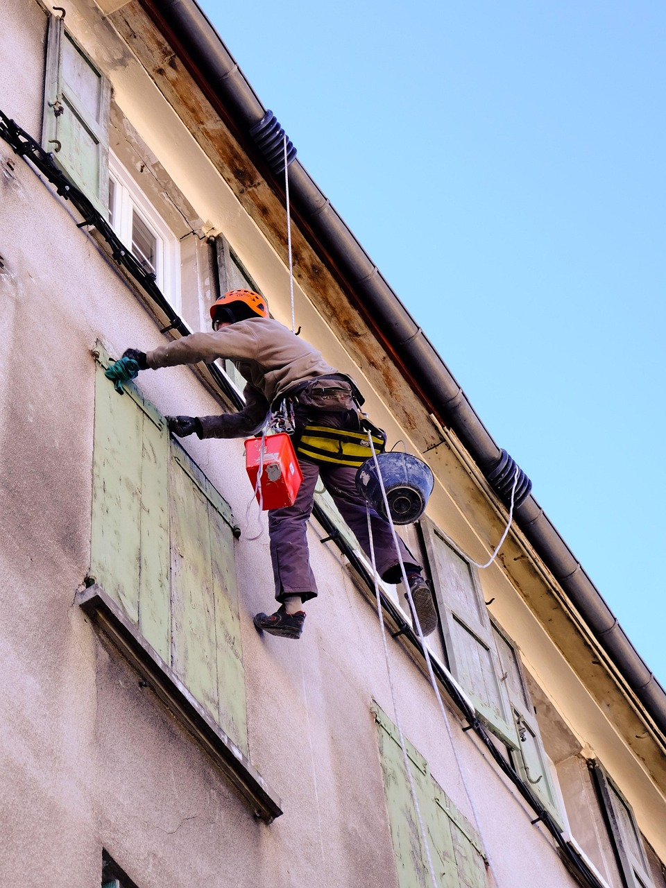 Roofing professional working with safety equipment on the exterior of a building for roofing services in Boulder, CO