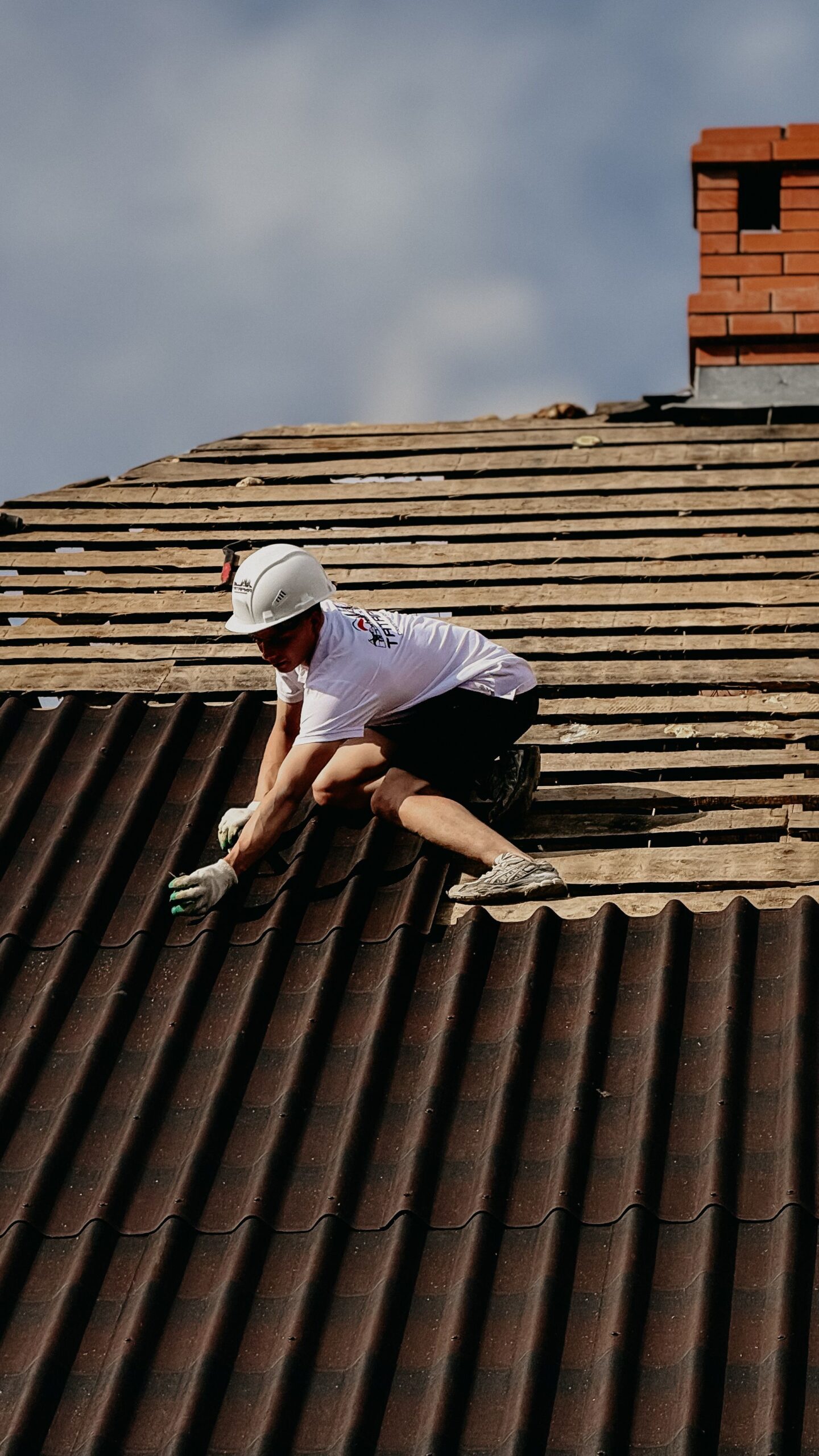 A construction worker installs roofing tiles wearing protective gear on a sloped rooftop for Professional Roofing Repair near me